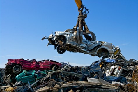 A crane transports a vehicle at a scrap yard