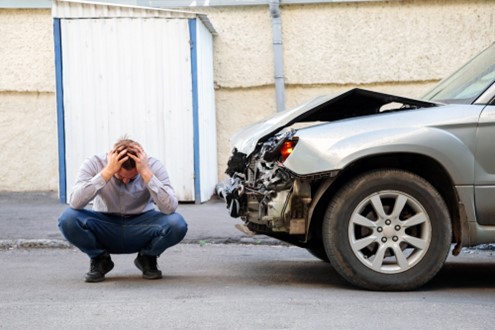 Man crouches in despair after his car is damaged in an accident